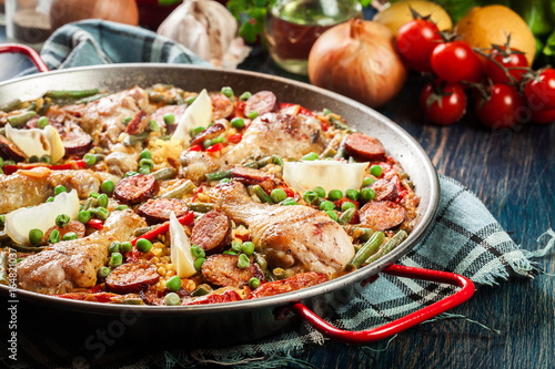 Traditional paella with chicken legs, sausage chorizo and vegetables served in paellera