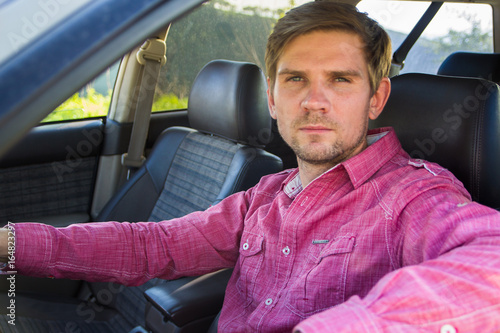 Handsome young man in a shirt driving a car