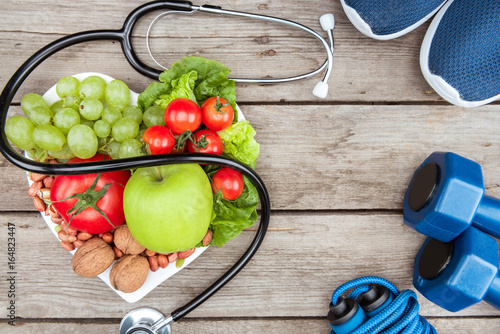 Fototapeta Naklejka Na Ścianę i Meble -  top view of stethoscope, organic vegetables and fruits and sport equipment on wooden surface, healthy lifestyle concept