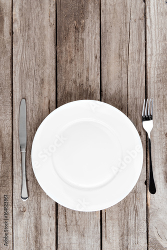 top view of arranged empty plate, fork and knife on wooden table
