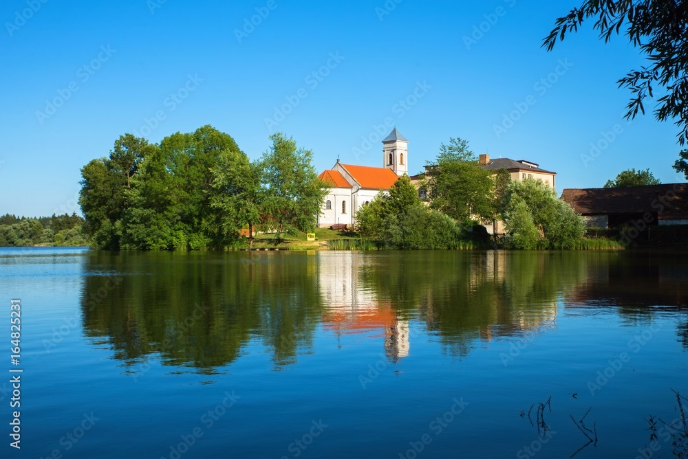 Village church with tree on shore of pond, Czech republic, Blato.