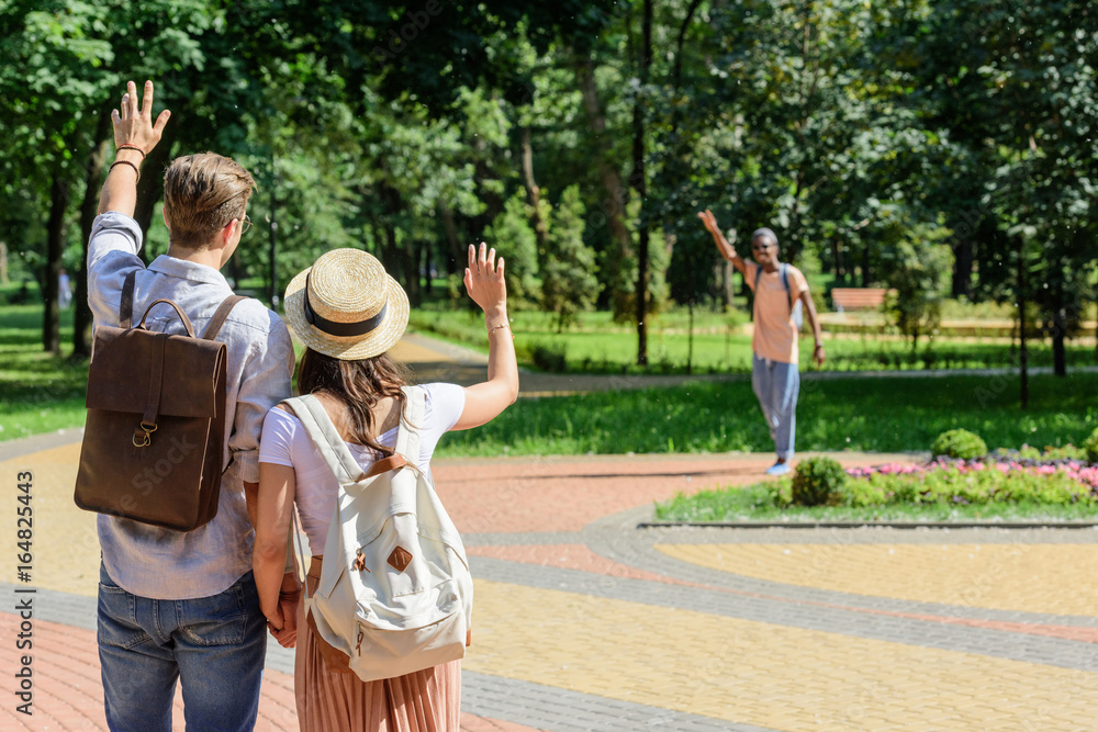 back view of couple waving to african american man in park