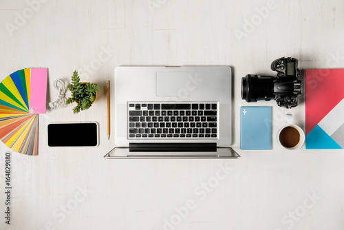 Work space for photographer, graphic designer. Flat lay of laptop, camera, colorchart, digital tablet, coffee cup, book, pencil on wooden table.