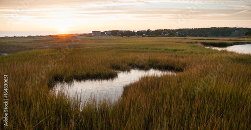 Sunset on Cape Cod with tide pool and marsh grasses in foreground.