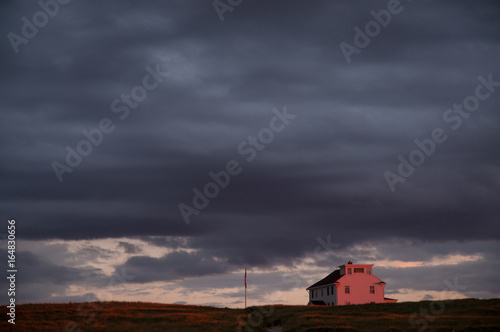 Dark clouds at dusk surround small house on horizon.