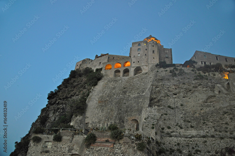 The Aragonese castle against the evening sky with glowing windows