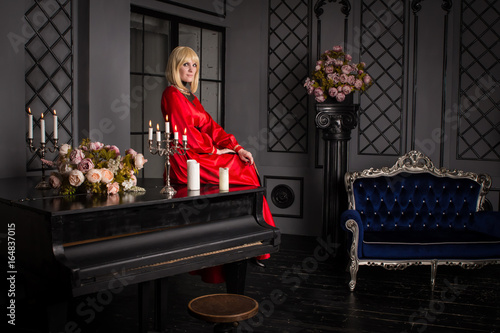 Beautiful blond woman sitting on the couch. She is dressed in a luxurious, expensive, red dress.