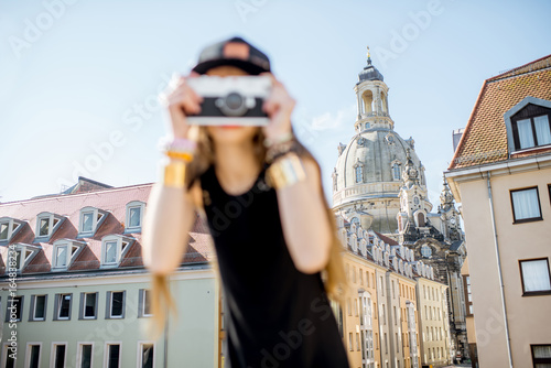 Young woman tourist standing with photo camera on the famous Bruhl terrace with great view on the old town in Dresden, Germany. Image focused on the background photo