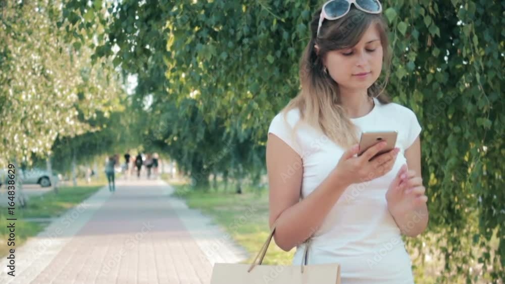 A young woman calls to thank for the service successfully stinted with shopping bags in sunglasses walking down the street with a smile