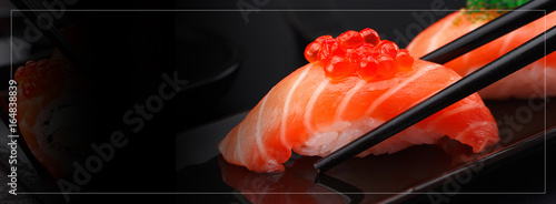 Japanese cuisine. Salmon sushi nigiri in chopsticks over black background.