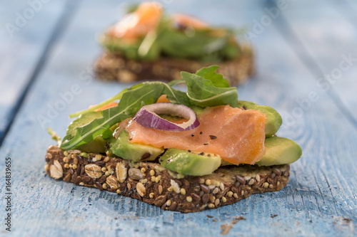 Countrybread Avocado, salted salmon sandwich with fresh herbs on blue craked paint wooden board background. Healthy eating theme photo