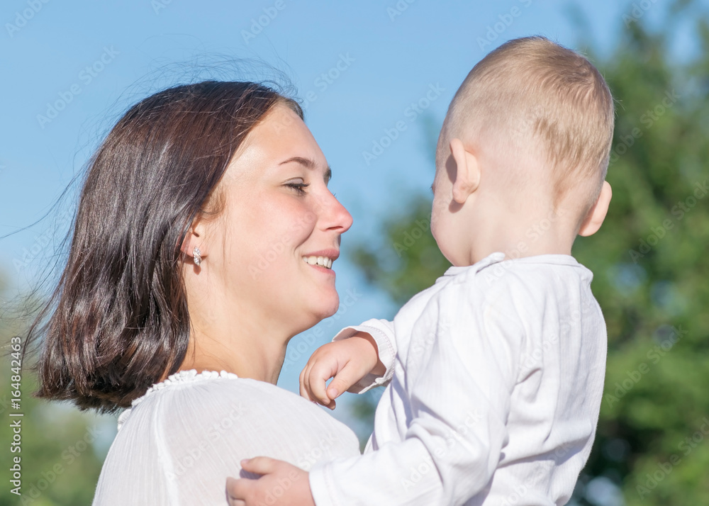 Young beautiful mother Holding child in her arms on nature in summer. Pretty woman looking with love on her baby son Young beautiful mother Holding child in her arms on nature in summer. Pretty woman looking with love on her baby son