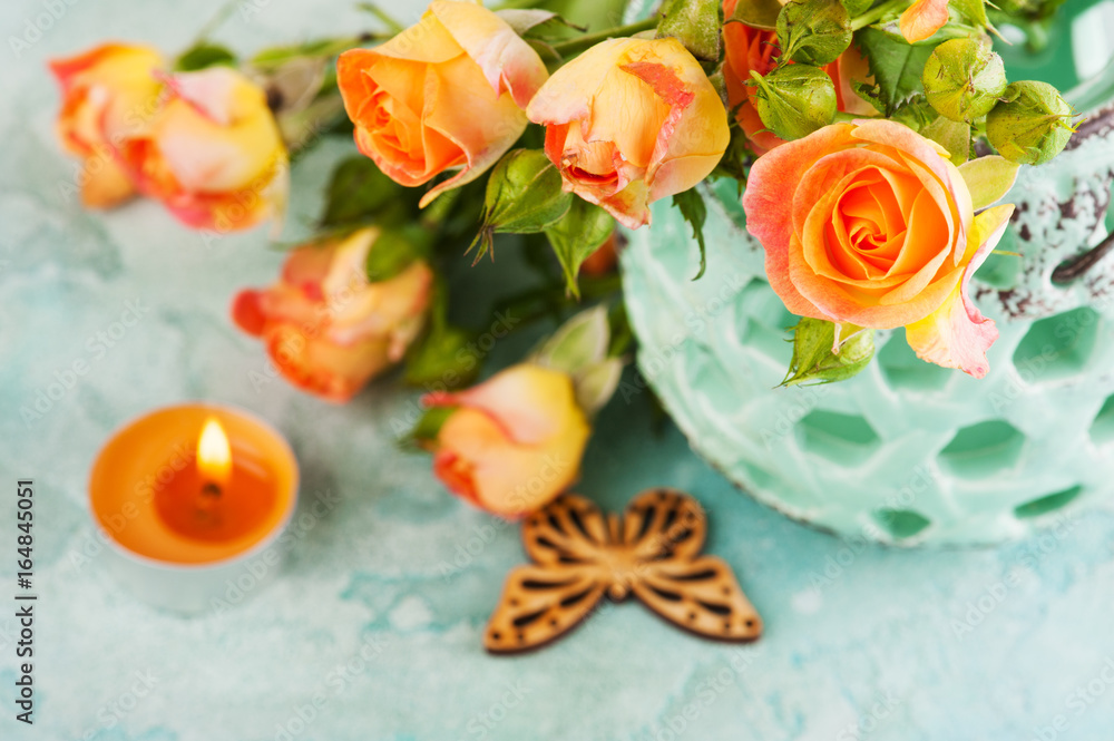 Fresh orange roses flowers in mint vase and lit candle