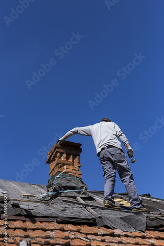 Roofer next to the chimney verifying the tiles and repairing the roof.