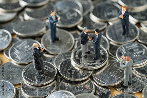 Fototapeta Naklejka Na Ścianę i Meble -  Miniature people: small figure businessmen handshaking and others clapping on stack of coin as money and financial agreement concept