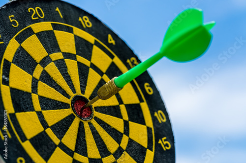 Business goals or target concept with selective focus on a dart pin in the center of dartboard with blue sky background