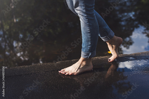 Barefoot woman in blue jeans walking on a water edge on a wet pavement