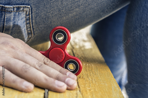 Closeup of a young caucasian man playing with a new red fidget spinner on a yellow wooden background and blue jeans photo