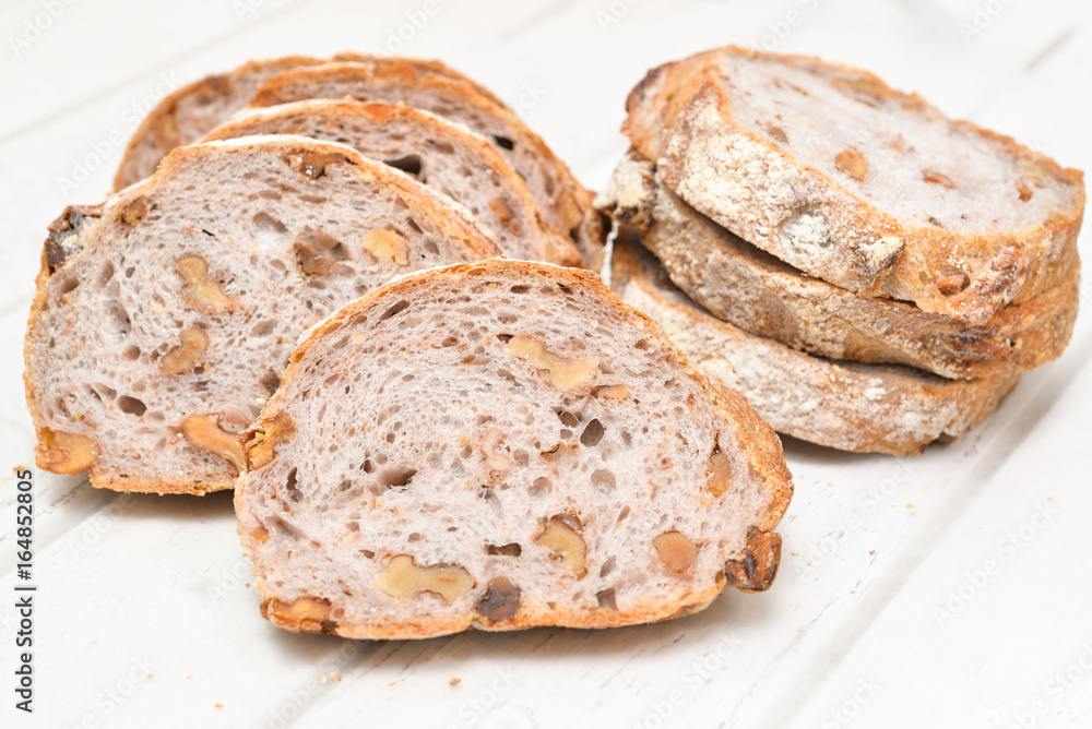 Slices of walnut bread on white wooden background