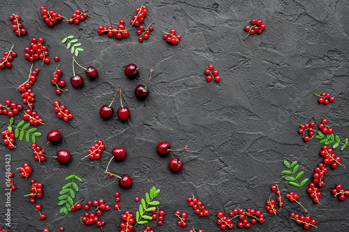 Berry theme. Red currant, cherry and leaves on black table background top view copyspace