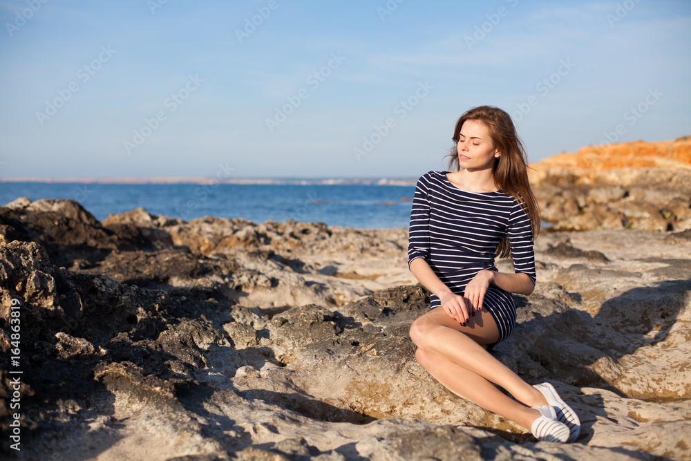 girl sits on the rocky beach enjoys sunshine