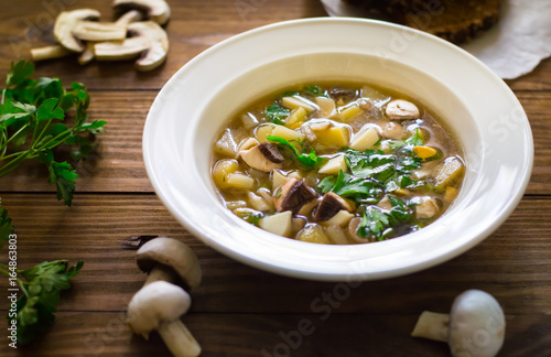 Delicious soup with wild mushrooms, potatoes, greens and cream. Wooden background. Top view. Close-up