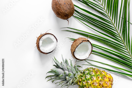 Concept of summer tropical fruits. Pineapple, coconut and palm branch on white background top view copyspace
