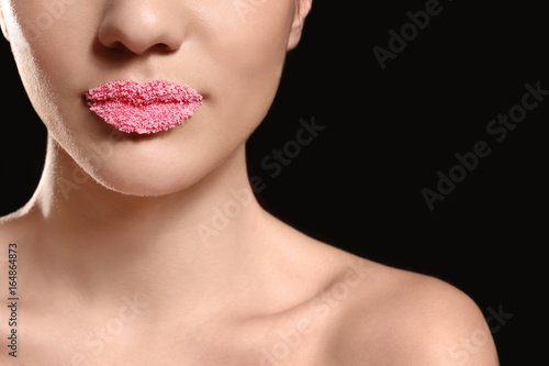 Lips of beautiful young woman covered with sugar on dark background, closeup
