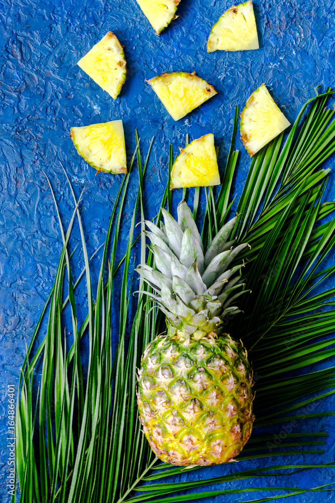 Fototapeta Ananasa i palmy gałąź na błękita stołu tła odgórnym widoku