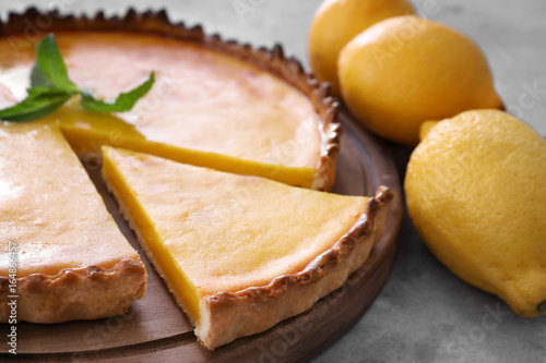 Wooden board with delicious lemon pie on gray table, closeup