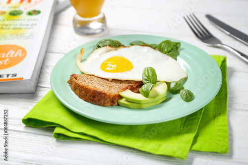 Delicious over easy egg with bread, avocado and basil leaves on kitchen table