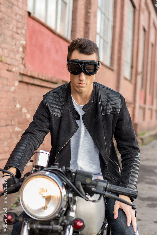 Homme Beau Biker Rider En Veste De Cuir Noir Et Jeans Mis Casque Près De La  Moto De Style Classique Café Racer. Vélo Fait Sur Mesure Dans Le Garage  Vintage. Style De