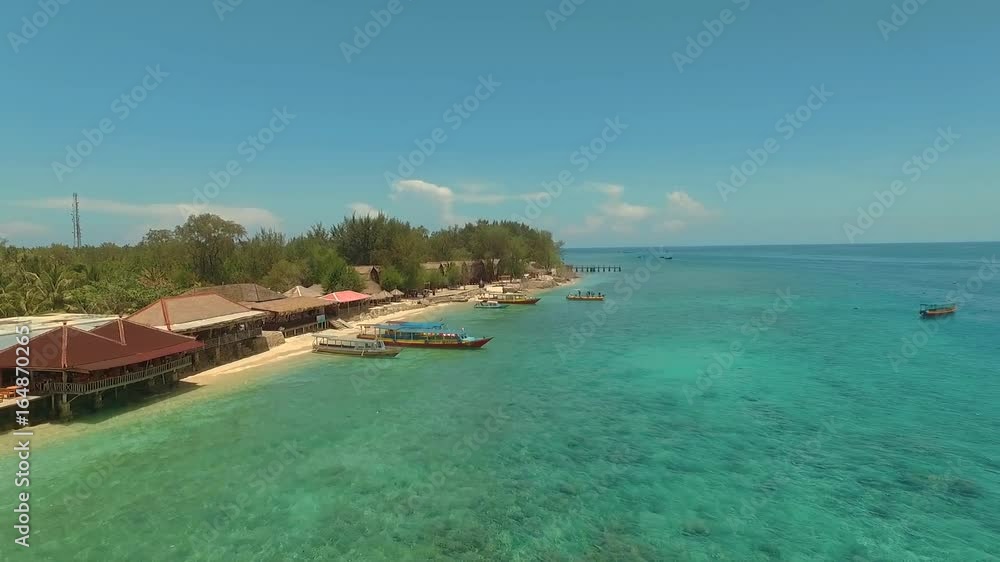 Aerial view of Gili Meno Island flying towards beach and small houses and huts, past boats and beachfront restaurants Aerial view of Gili Meno Island flying towards beach and small houses and huts, past boats and beachfront restaurants