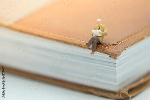 Reading and hobby concept. Miniature mini figures male sitting on a big book and reading a book. photo