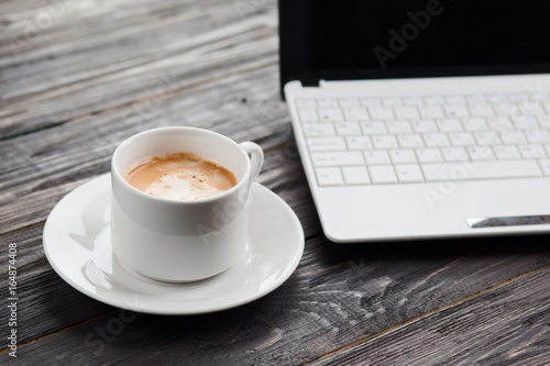 Coffee cup close up and laptop on wooden table