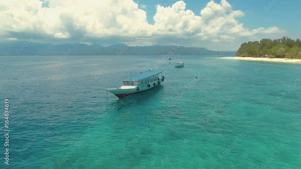 Flying around a boat near Gili Meno Island with perfect turquoise water on a sunny summer day, aerial view with Lombok mountains in background Flying around a boat near Gili Meno Island with perfect turquoise water on a sunny summer day, aerial view with Lombok mountains in background
