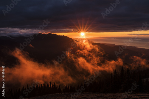 Canvas Print sun setting over the ocean with big mountains on the coast