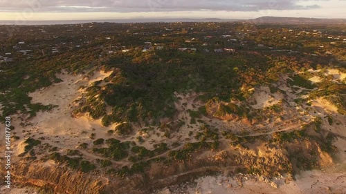 Forward flight over ocean and coastline toward rural houses among coastal vegetation at sunset