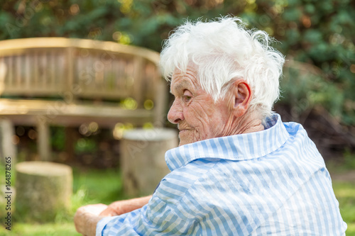 Profil einer Seniorin, sitzt in ihrem Garten und schaut nachdenklich nach links