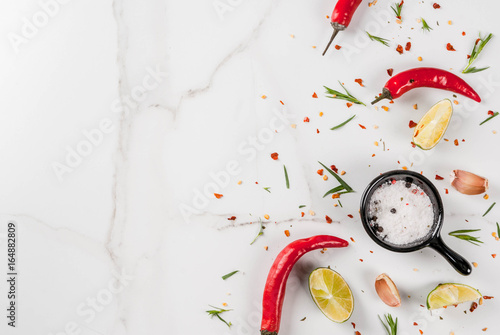 Cooking food background, White marble table with spices - hot red pepper, seasonings, garlic, salt, greens, tarragon, parsley, herbs, lime lemon, top view copy space