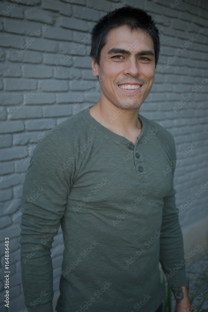 Obraz premium Handsome Smiling Ethnic Man in Front of Brick Wall