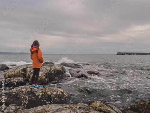 Young girl in orange coat watching waves  West Coast of Ireland.