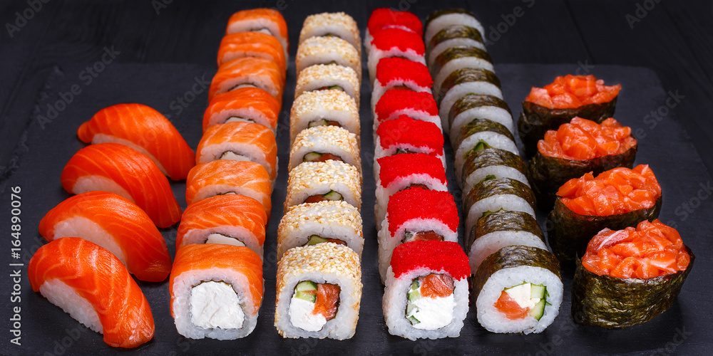 Appetizing maki and nigiri sushi set, served on black stone slate. Restaurant menu, Japanese food art. Appetizing maki and nigiri sushi set, served on black stone slate. Restaurant menu, Japanese food art.