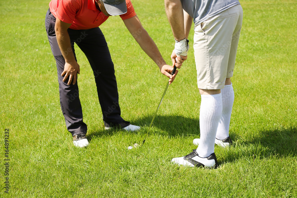 Obraz premium Caddy teaching young man to play golf on course in sunny day