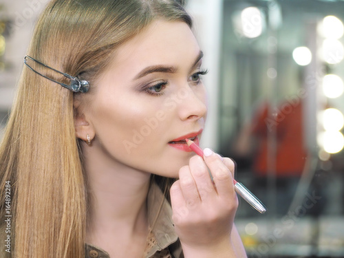 Make-up artist makes make-up at the female models lips bright close-up