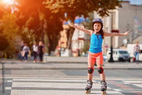 Funny Little pretty girl on roller skates in helmet riding in a park.