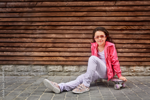 Stylish little girl child wearing a summer or autumn pink jacket, white jeans, sunglasses © Aleksey