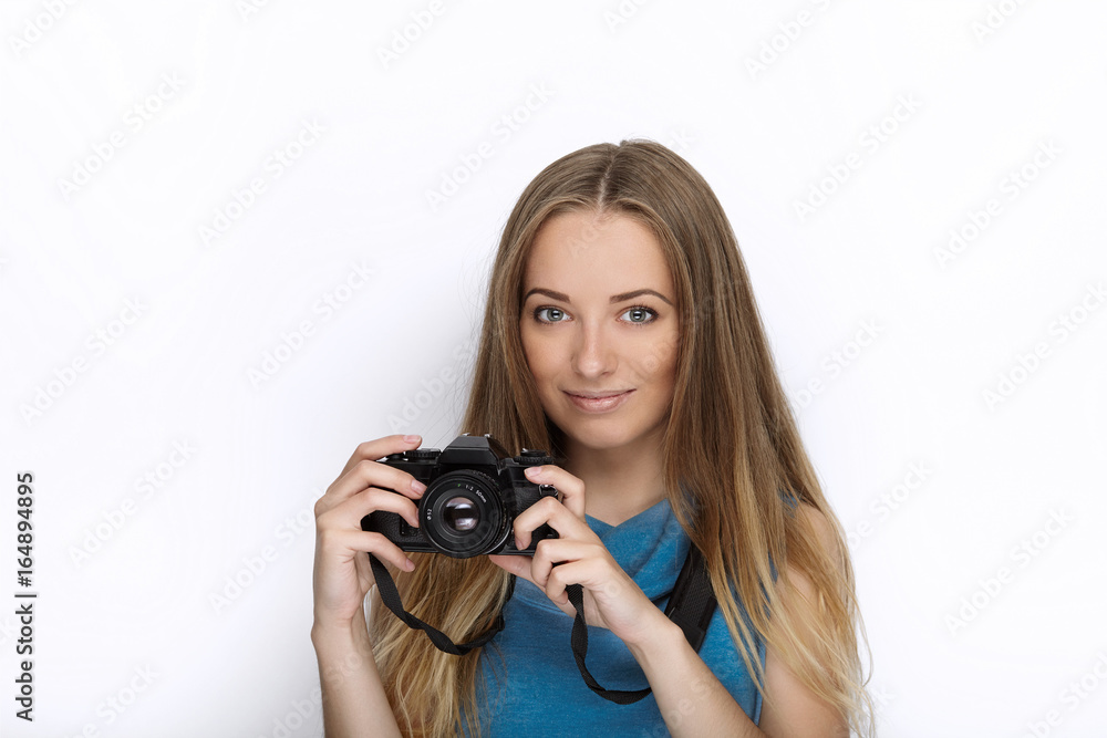 Headshot of young adorable playful blonde woman with cute smile in cobalt color blouse posing with black dslr camera on white backdrop