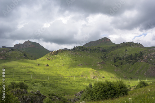 Горный пейзаж, красивые зеленые склоны в живописном ущелье, облачное небо. Природа и горы Северного Кавказа