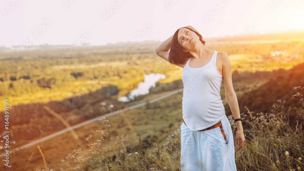 Beautiful pregnant woman doing prenatal yoga on nature outdoors.